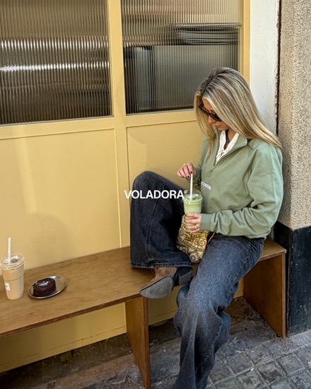 Anuncio de Voladora: foto UGC de una chica con sudadera verde tomando café en un banco
