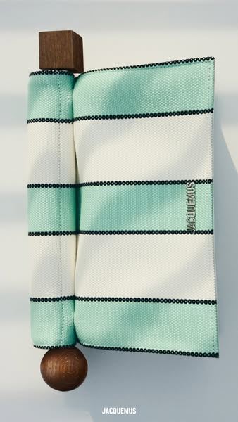 Anuncio de Jacquemus: bolso de rayas verdes y blancas colgado entre dos piezas de madera, como un bodegón