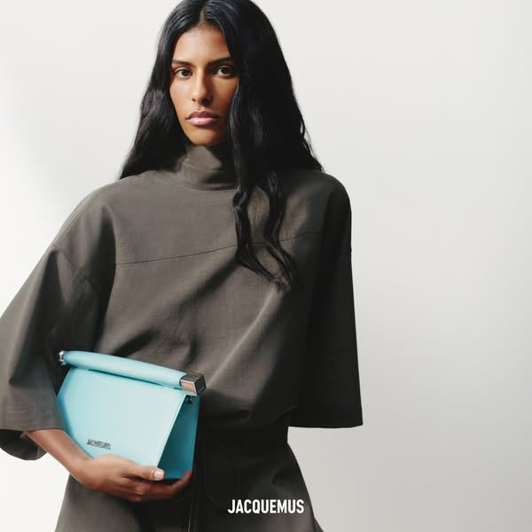 Anuncio de Jacquemus: modelo con jersey marrón y un bolso azul claro, foto de estudio sobre fondo blanco