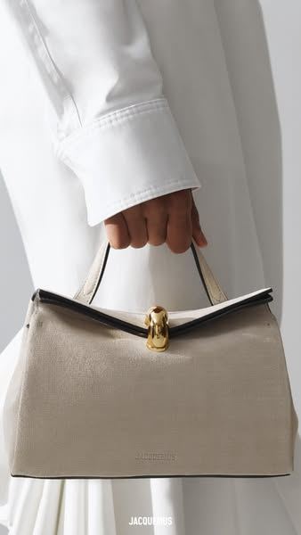 Anuncio de Jacquemus: mano sujetando un bolso beige con cierre dorado sobre un fondo blanco